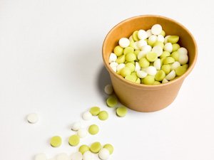 Pequeños wax melts de la marca Velecia, con aroma a manzana y melocotón, en colores blanco y verde, dentro de una tarrina de cartón kraft, con algunos wax melts esparcidos alrededor.